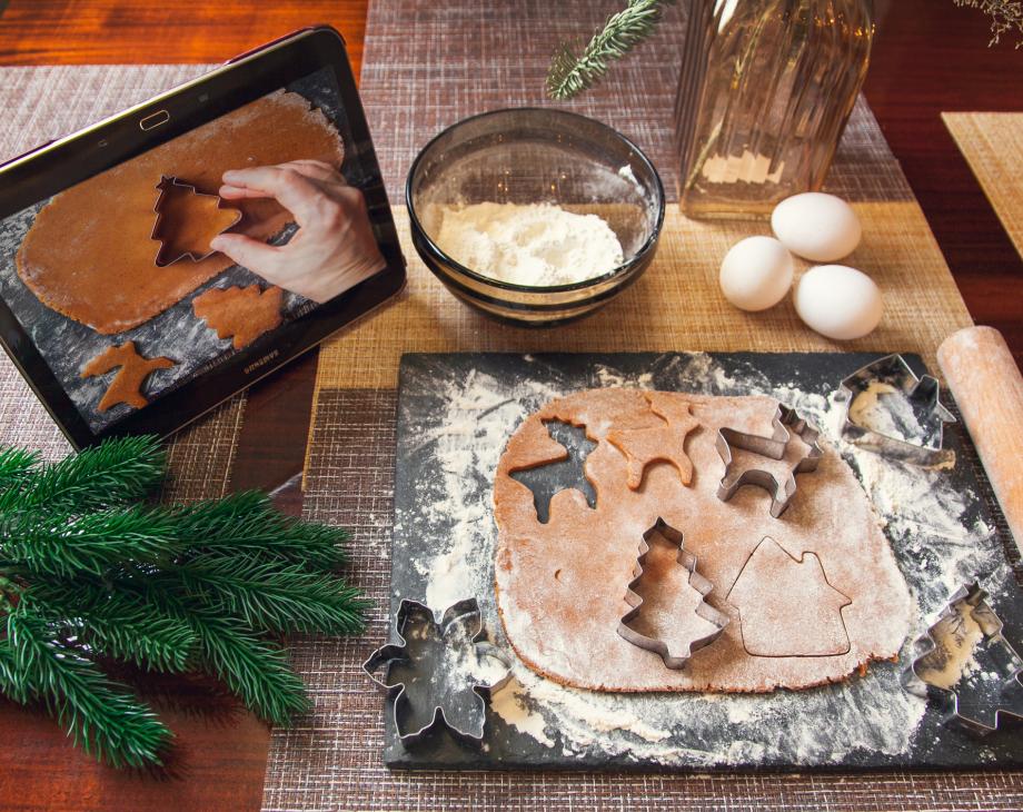 Baking station with cookie dough and cutters, rolling pin, eggs, flour and a tablet showing the recipe