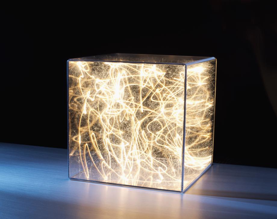 Color photo of transparent cube filled with a jumbled mass of lit strings of light